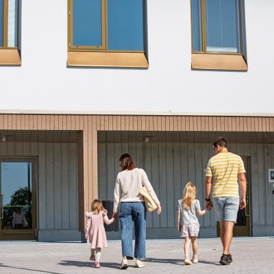 Äiti ja isä vievät lapsiaan päiväkotiin ja pitävät heitä käsikädestä.