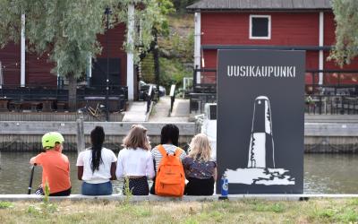 Lapset istuvat uudenkaupungin kaupunginlahden rannalla selkä kameraan päin. 