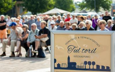 Yleisö istumassa torilavan edessä penkeillä.