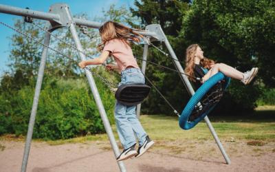 Lapsi ja teini-ikäinen tyttö keinuvat leikkipuistossa kesällä.