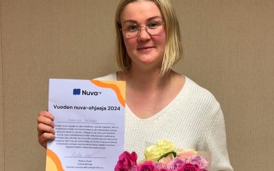 Vaalea nainen pitelee kukkia ja kunniakirjaa