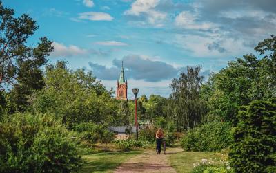 Tyttö taluttaa pyörää Myllymäen puistossa, taustalla näkyy uuden kirkon torni