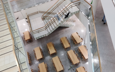 Portaikkoa ylhäältä alaspäin kuvattuna ja alhaalla tammen värisiä ruokapöytiä tuoleineen.