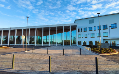 Edessä uusi moderni rakennus, jossa valkoista rapattua pintaa ja toisessa sivussa isot lasiseinät vinoine kattoineen.