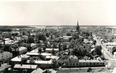 sisällön kuvaus: Valokuvapostikortti. Yleisnäkymä kaupungista, Myllymäen vesitornista kuvattuna. Etualalla Myllykatu, oikealla Vuorikatu, vasemmalla Ylinenkatu ja museo. Taustalla uusi ja vanha kirkko. Kaupunkikuva
