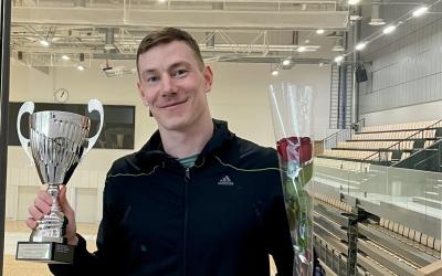 mies pitelee pokaalia ja ruusua, taustalla liikuntahalli