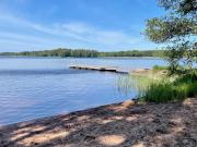 hiekkaranta ja järvimaisema, taustalla laituri ja lehtipuita