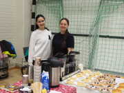 Kaksi nuorta naista katsoo hymyillen kameraan kahvilatiskin takaan. Edessä leivonnaisia.