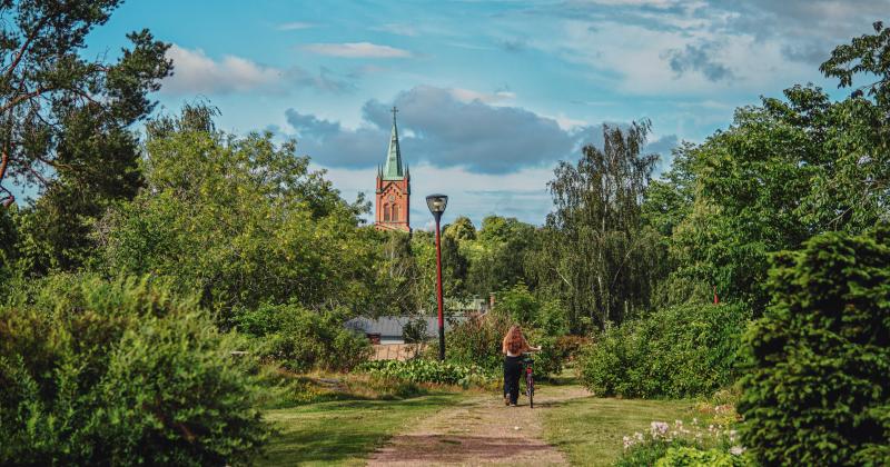 Tyttö taluttaa pyörää Myllymäen puistossa, taustalla näkyy uuden kirkon torni