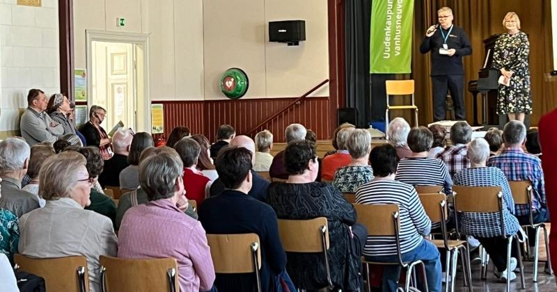 ihmisiä istuu salissa kuuntelemassa kahta ihmistä lavalla