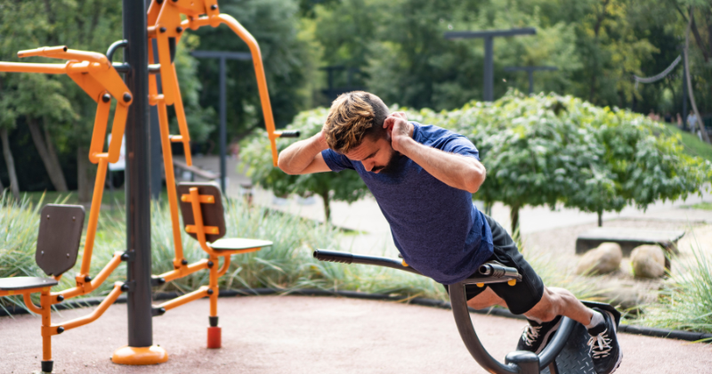 Mies kuntoilee ulkokuntosalilla, tekee selkälihaksia. Taustalla näkyy ulkokuntosalilaitteita.