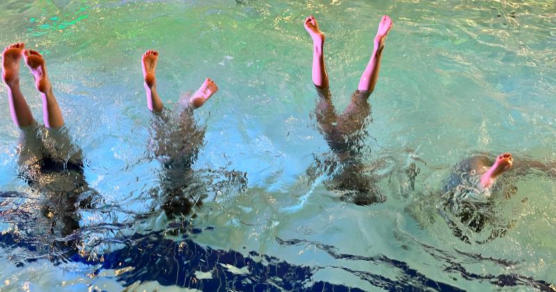 4 tyttöä seisoo käsillä uima-altaassa, varpaat pinnalla