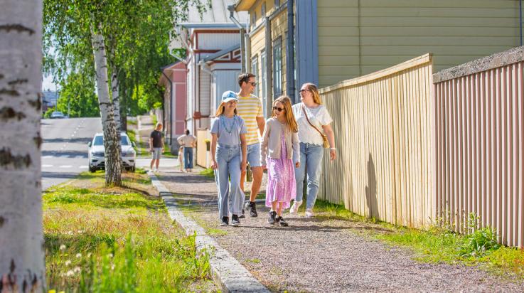 Perhe kävelemässä puutalokadulla