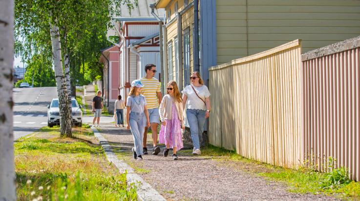 Perhe kävelee puutalokadulla