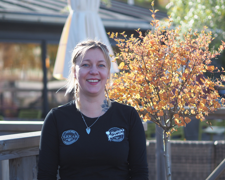 Reija Sallinen seiso ravintolansa edessä, hymyilee ja katsoo kohti.