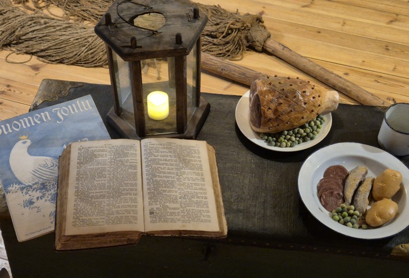 merimiehen joulukattaus kirstun päällä, Raamattu, kynttilälyhty, kinkku.